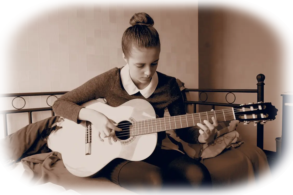 Молодая и красивая девушка играет на гитаре сидя на кровати