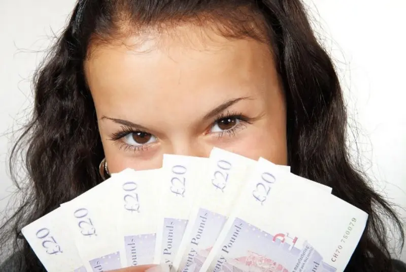 Девушка брюнетка с пачкой денег смотрит карими глазами
