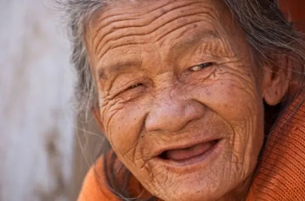 Древняя, седая старушка в оранжевой кофте по доброму улыбается беззубым ртом